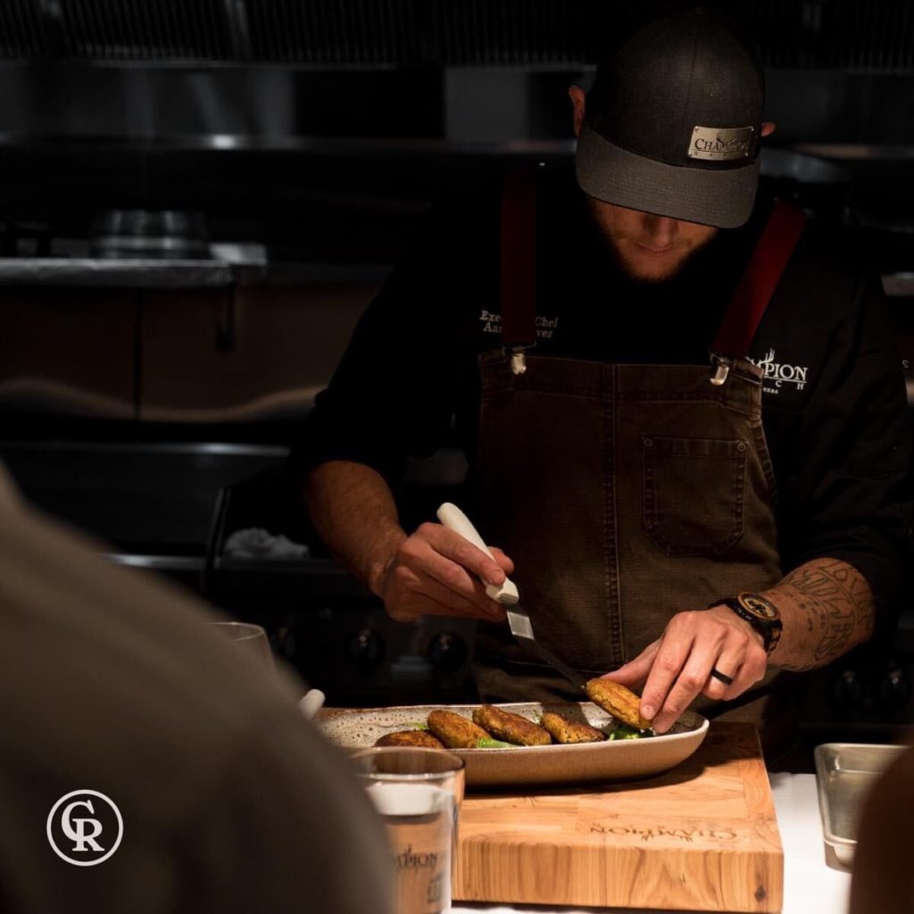 Champion Ranch Chef plating grilled food while wearing a custom metal badgecap with their business logo