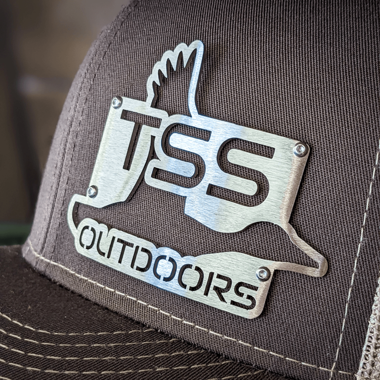 Close up of brushed stainless steel laser cut badgecaps badge featuring TSS Outdoors logo