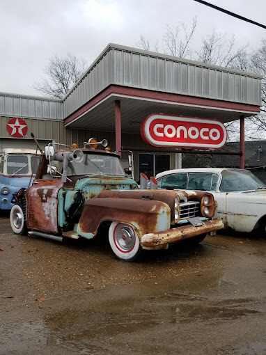 Photo of old rusty custom vehicles in front of a gas station Kraven Kustoms with a Cocnoco sign and a Texaco star sign