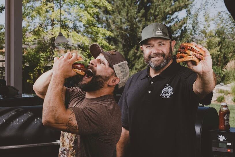 Chad Belding and friend holding burgers while wearing custom metal BadgeCaps featuring the Almond Beef Logo