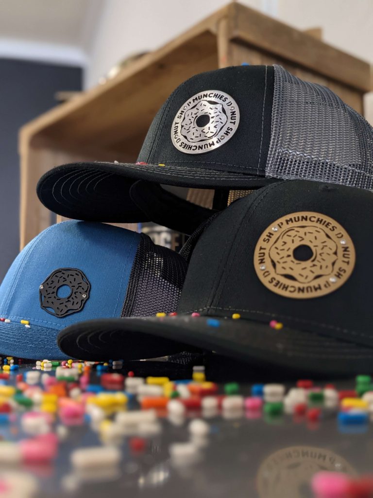 Stack of premium BadgeCaps custom metal hats with Munchies Donut Shop Logo