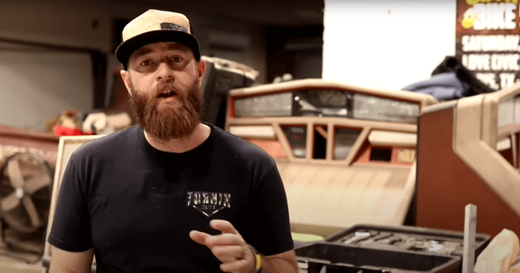 Freeze frame of Lance Bush of Kravened Kustoms wearing a shirt featuring the Turnin' Rust Logo, and a laser cut metal BadgeCaps stainless steel badge